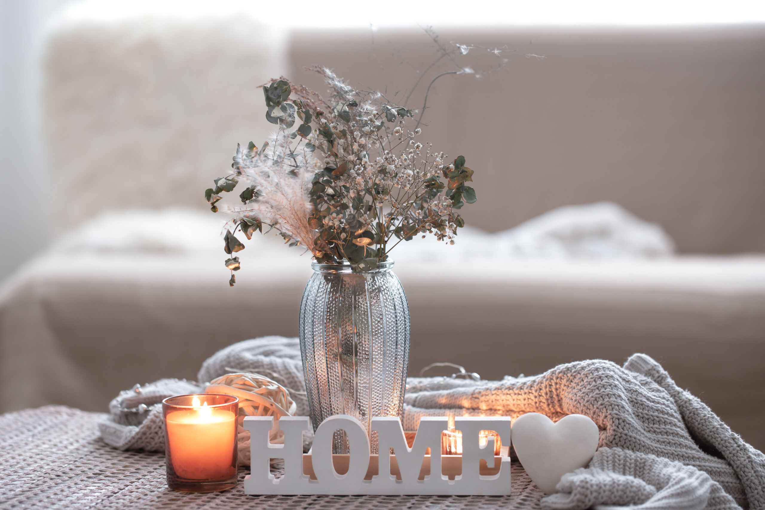 Cozy composition with decorative word home, candles and a vase with dried flowers in the interior of the room.